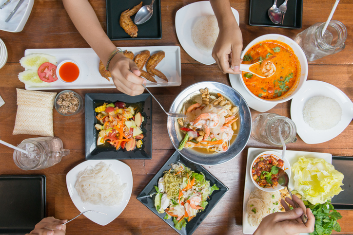 Top view of friends or family eating Thai food together on wood table.