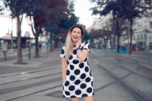 smiling woman in black and white dress in dots enjoying walk in the city.