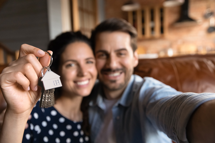 Crop close up portrait of happy Caucasian young couple show keys to new home or apartment feel excited moving in together. Overjoyed man and woman renters tenants celebrate relocation to new house.