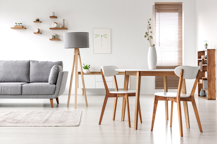 Wooden chairs at table in bright open space interior with lamp next to grey couch