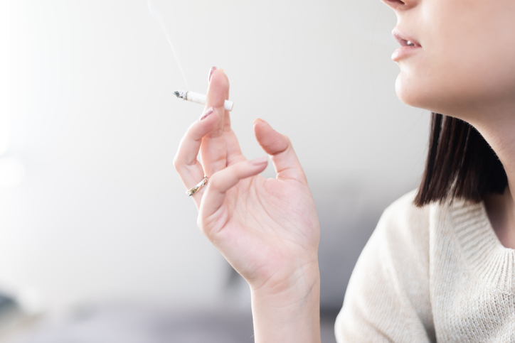 Joven milenaria malsana fumando un cigarrillo en un sofá en su apartamento
